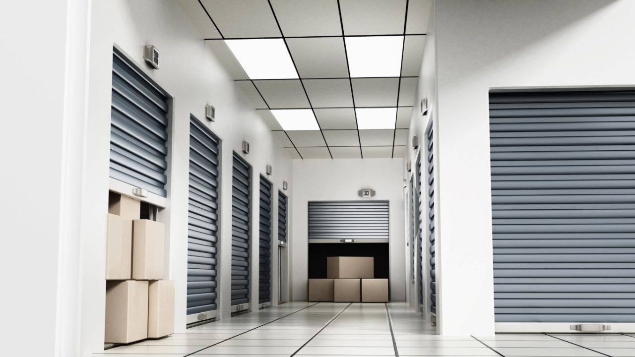 Open self storage units full of cardboard boxes among closed doors.